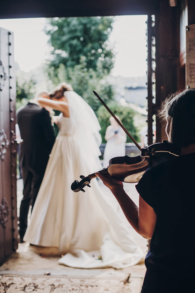 Violinist playing as bride and groom stand together at open doorway during wedding ceremony.
